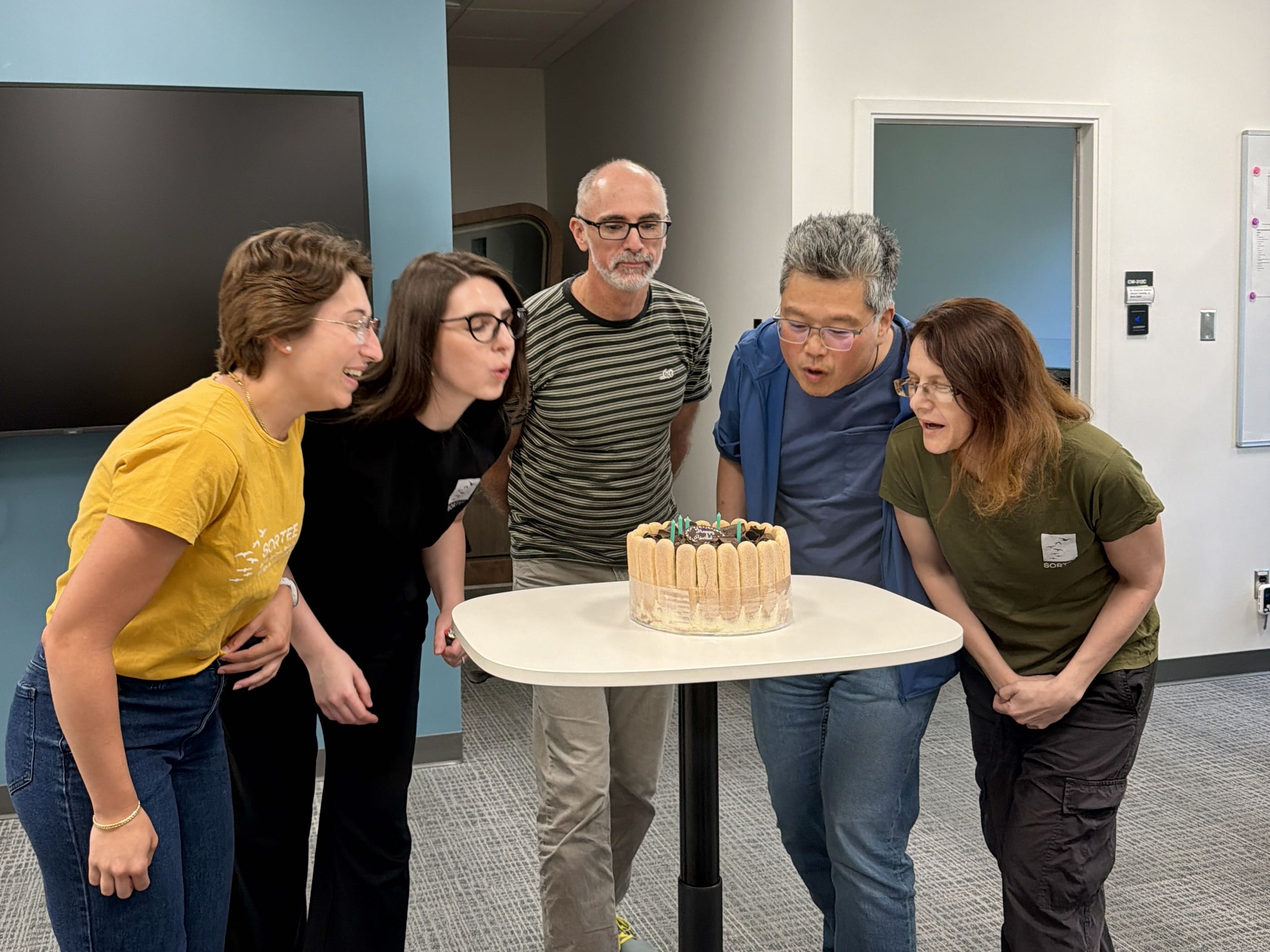 5 SORTEE members blowing out candles on a birthday cake